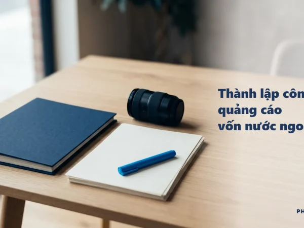 Thành lập công ty quảng cáo vốn nước ngoài: bìa hồ sơ navy, ống kính máy ảnh và bút xanh trên bàn
